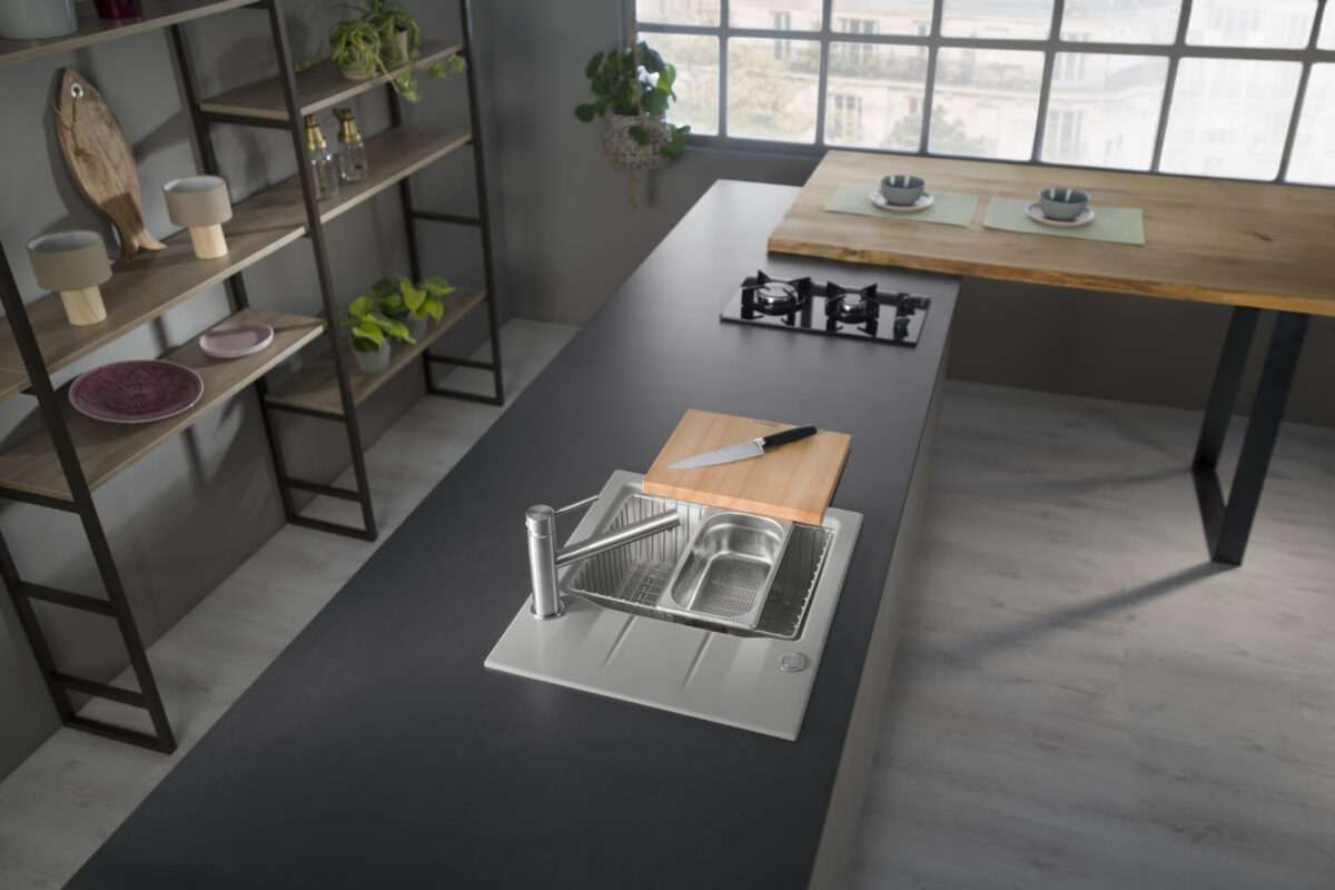 Systemceram sink with cutting board and integrated colander on a dark island in a loft-style kitchen.