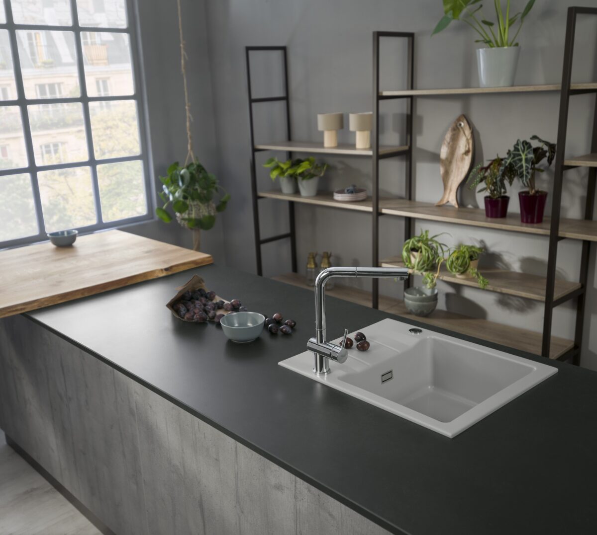 White Genea 60 ceramic sink by Systemceram in a dark kitchen island with shelving and large windows.