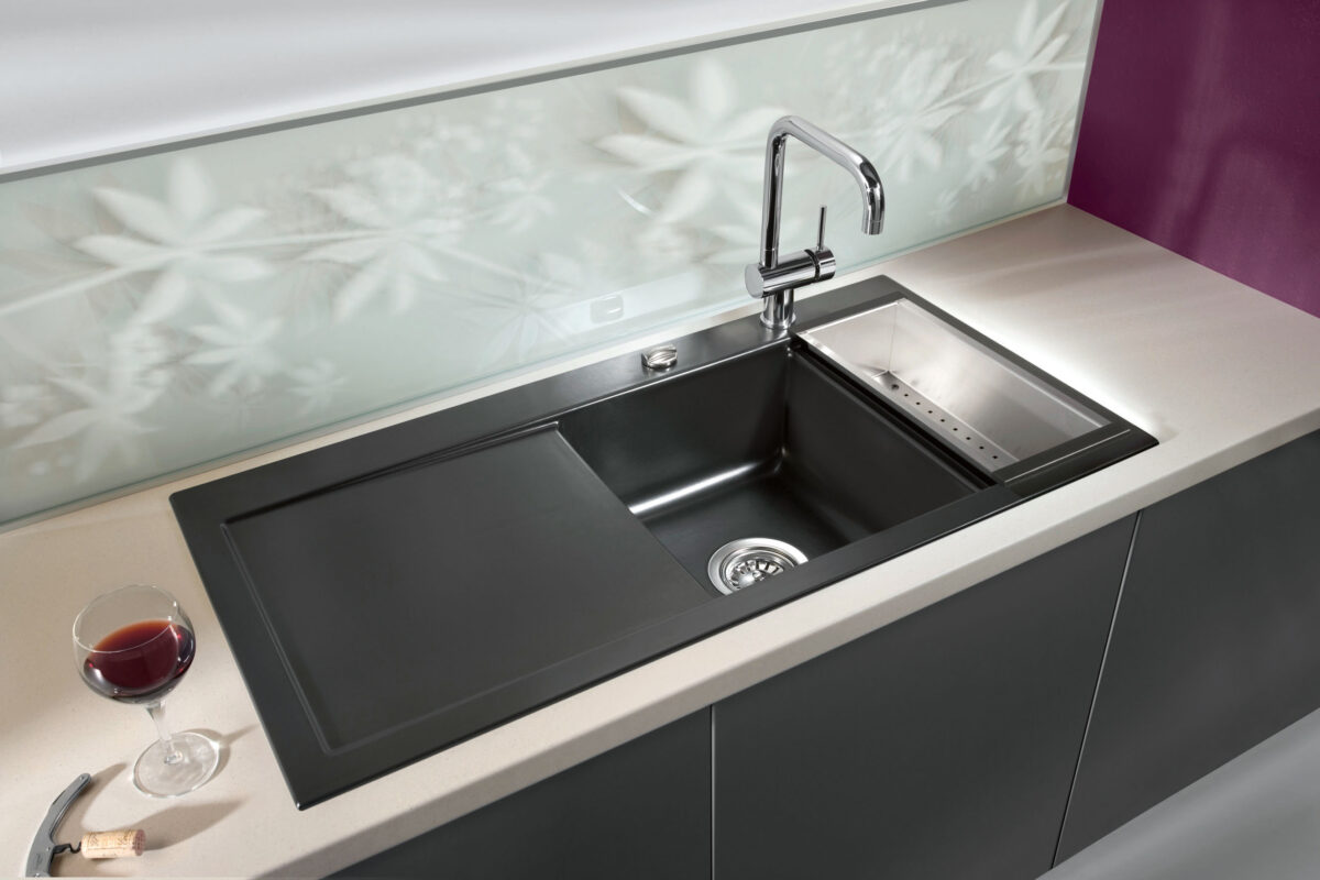 Black Systemceram sink with stainless-steel insert and glass cover in a modern kitchen with purple backsplash.