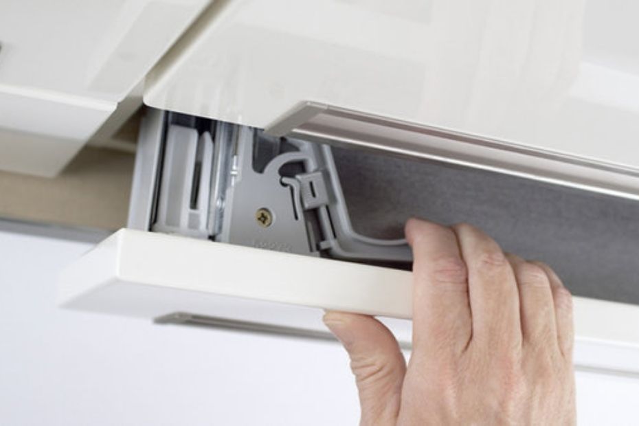 Close-up of a hand opening a kitchen drawer to reveal the concealed GRASS child safety latch mounted underneath.