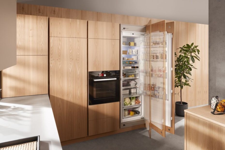 Tall built-in refrigerator with wooden front open to reveal organized shelves in a modern kitchen.