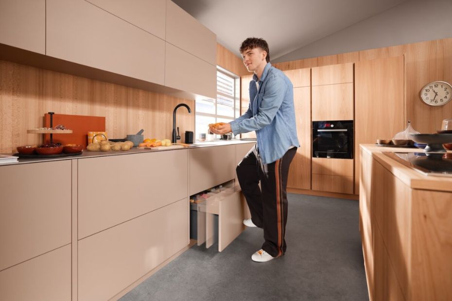 Person taps the waste pull-out with a knee to activate hands-free electronic opening in a modern kitchen.