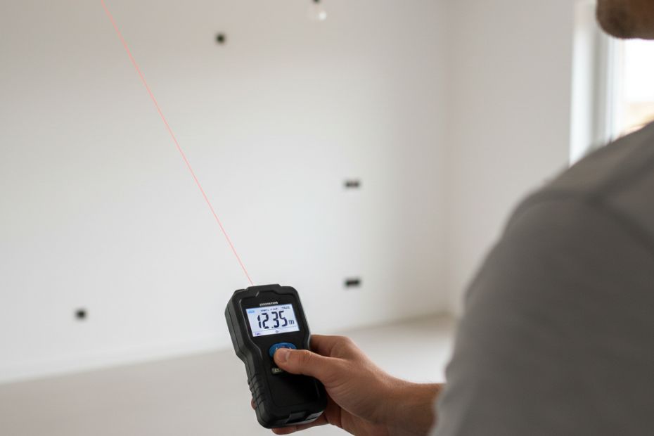 Person using a laser distance measurer to measure wall length inside a kitchen.